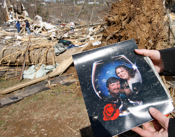 Charlotte Jones holds a photo of her sister Melissa Evans and Ricky Batey with the house Melissa died in, in the background near Crossville, TN